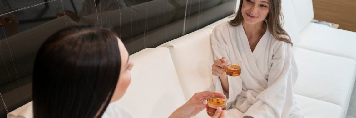 Two women in bathrobes enjoy tea together, embracing relaxation and self-care in a spa lounge.